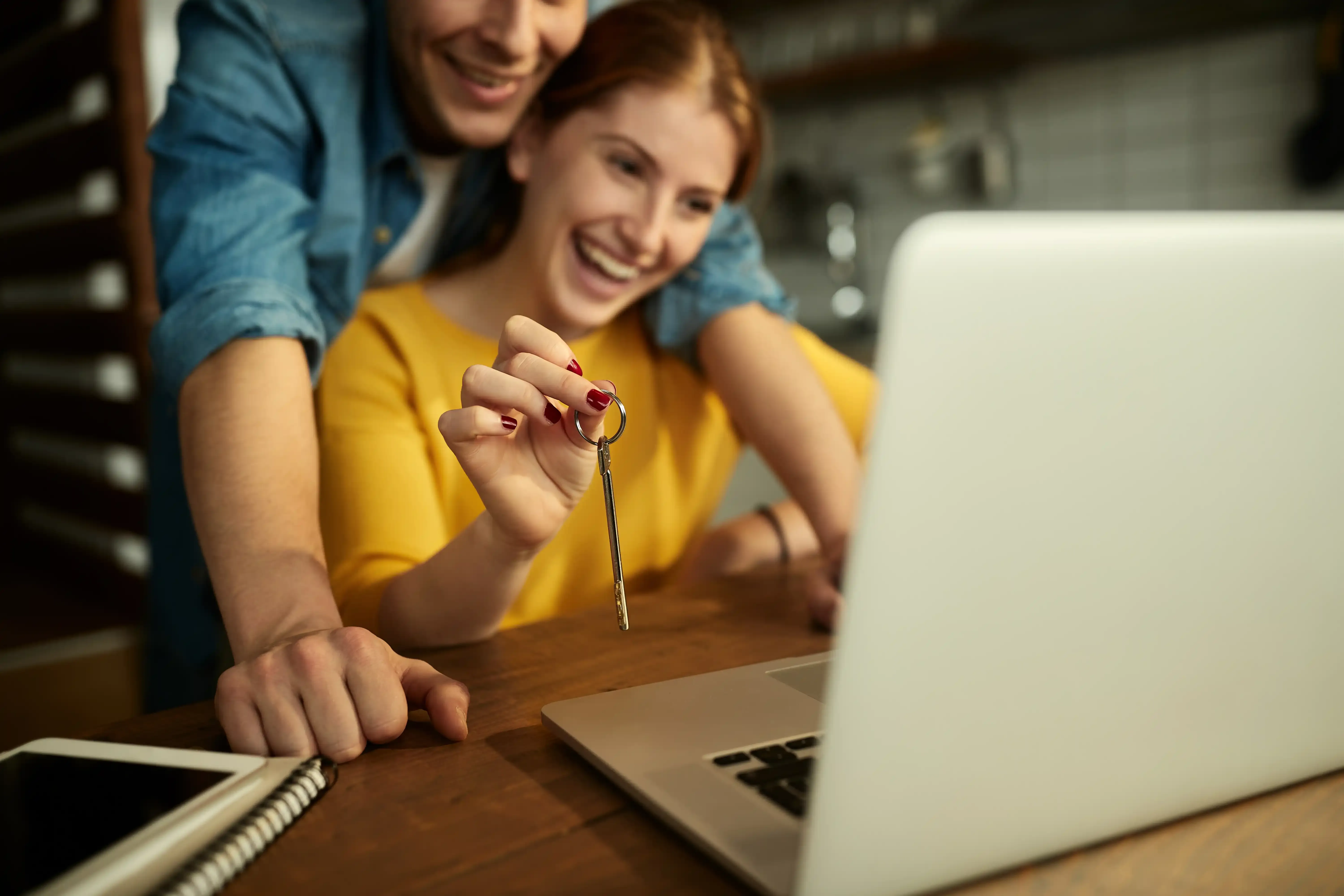 Jeune couple souriant devant un ordinateur cherchant une assurance habitation pas chère pour leur maison