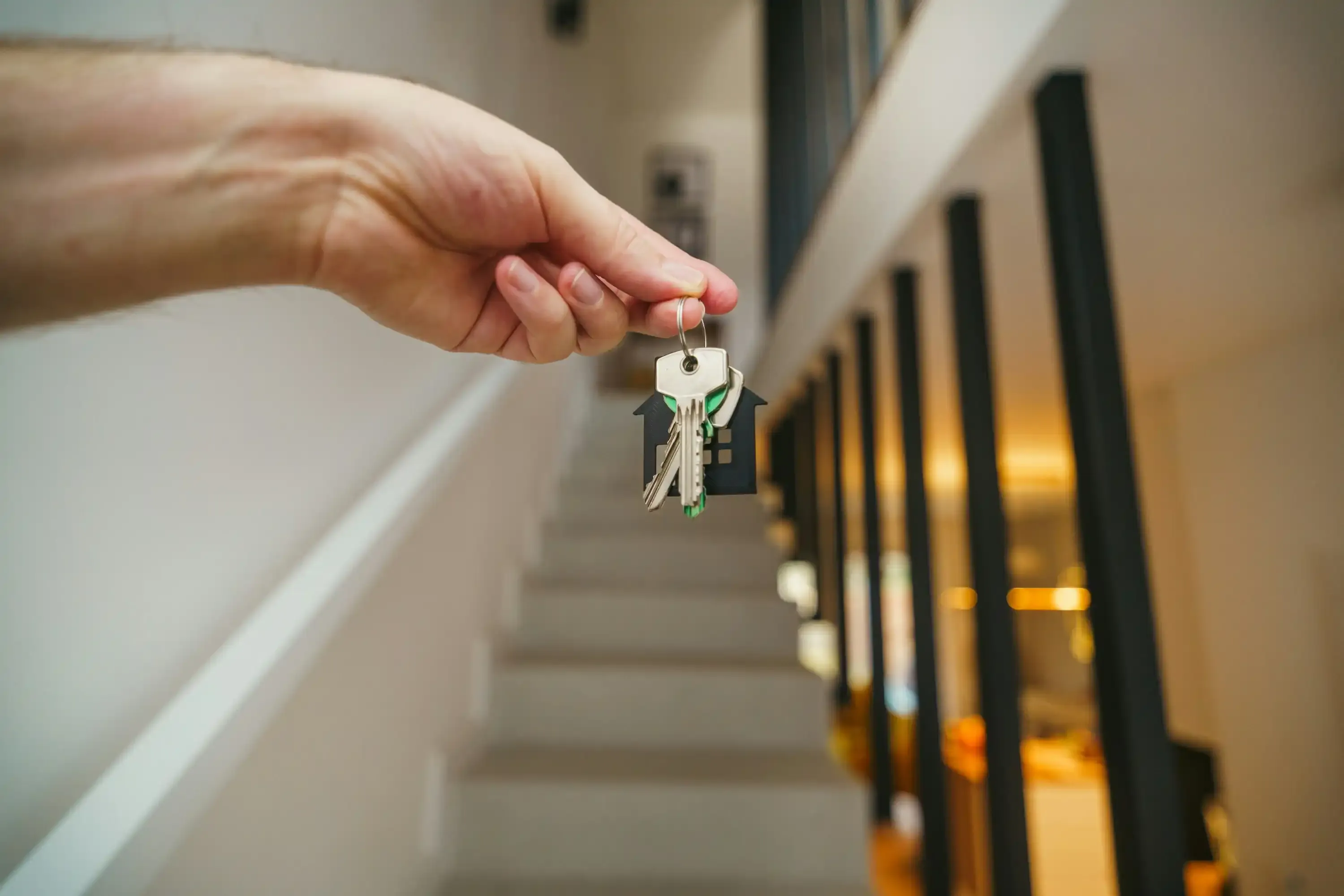 Main tenant un trousseau de clés avec porte-clés en forme de maison dans un intérieur moderne